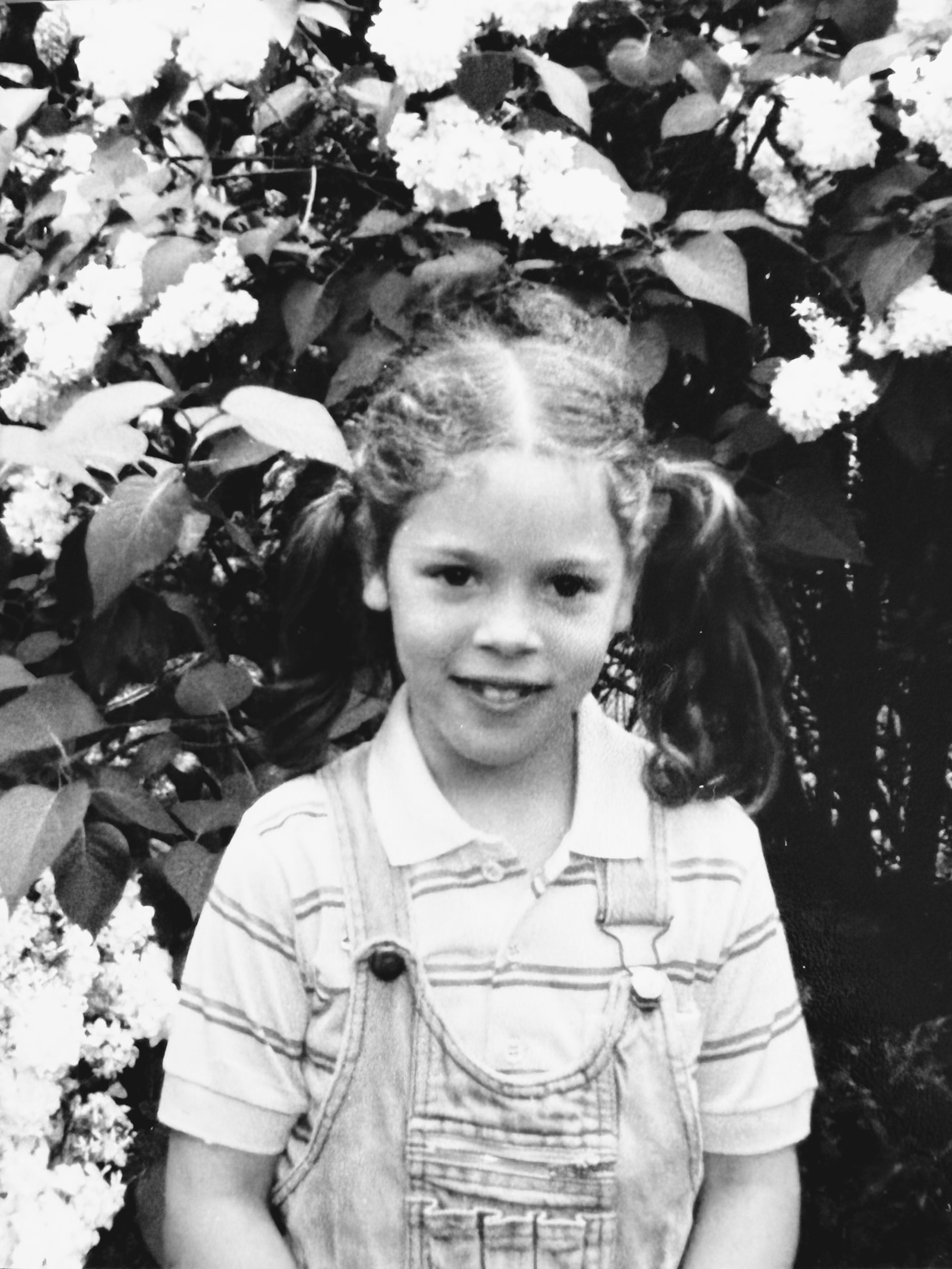 Lilian als kind met staartjes tussen bloeiende struiken